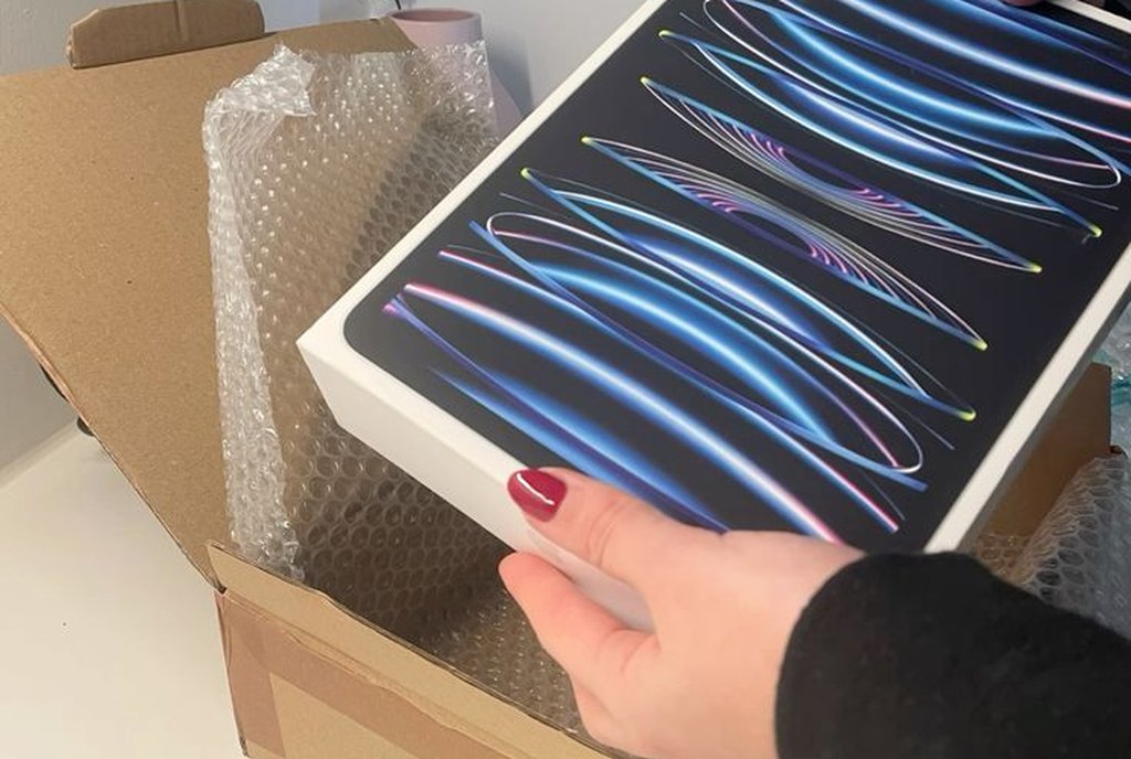 Mãos retirando um tablet grande de dentro de uma caixa de papelão sobre a mesa